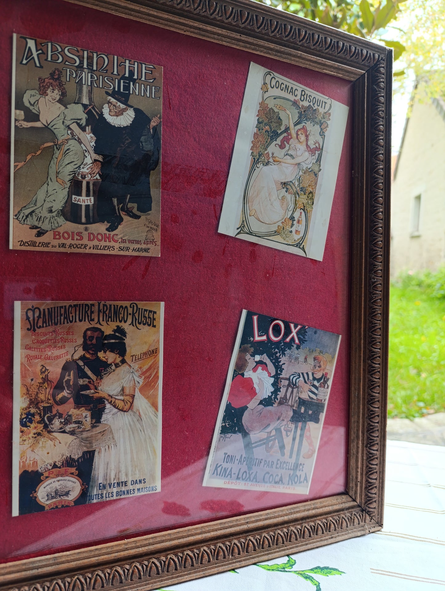 Cadre vintage 46 × 56 cm, poids 2,5 kg, contenant six reproductions d’affiches publicitaires anciennes sur fond rouge bordeaux.