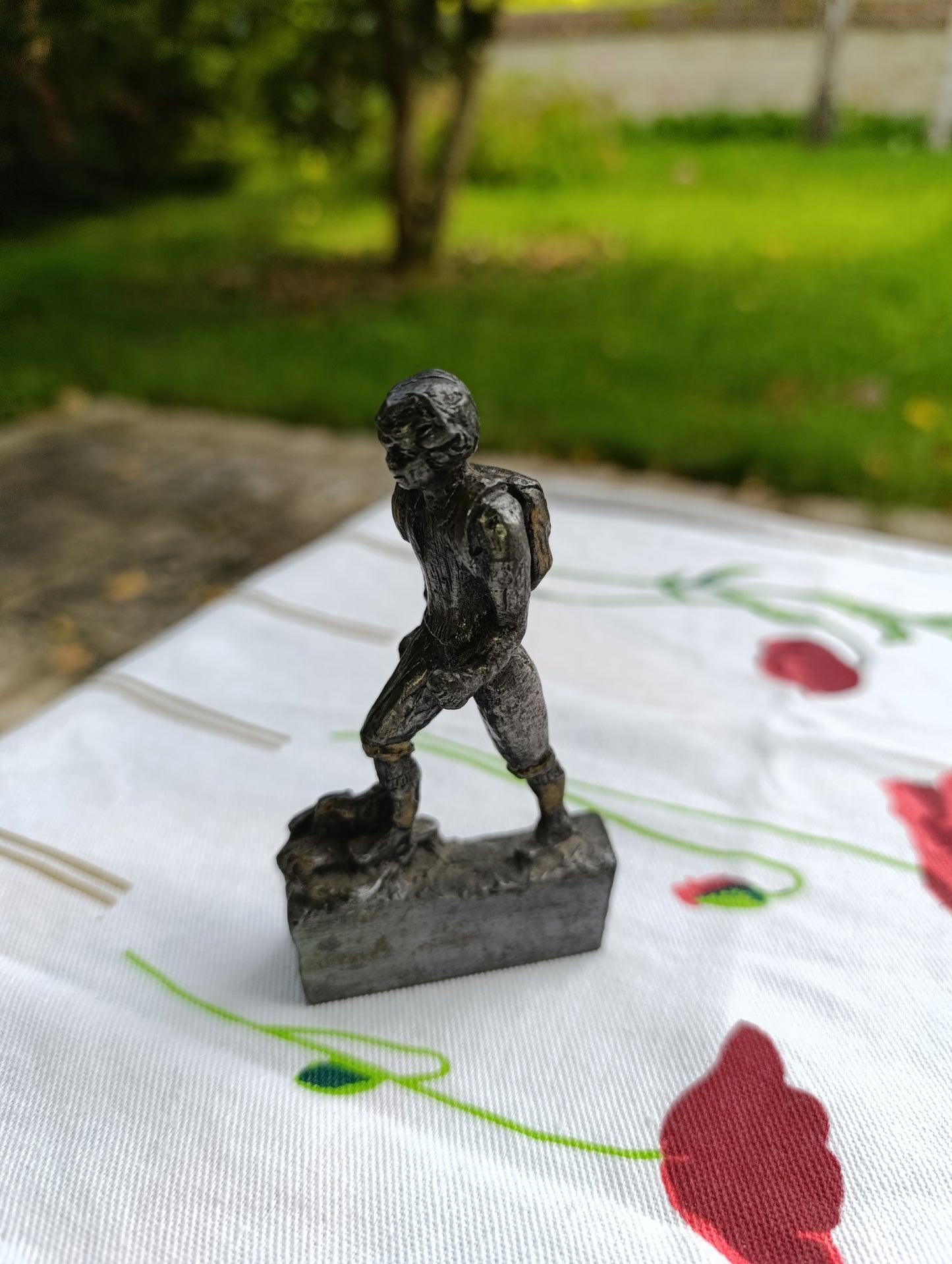Petite statuette en métal patiné représentant un joueur de football, posant le pied sur un ballon.