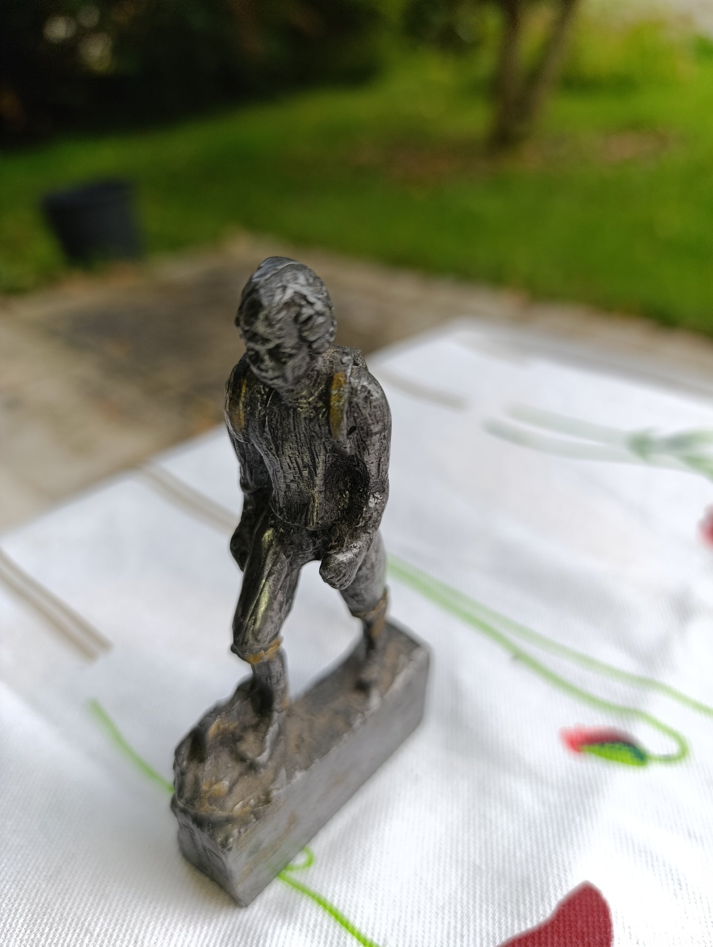 Petite statuette en métal patiné représentant un joueur de football, posant le pied sur un ballon.